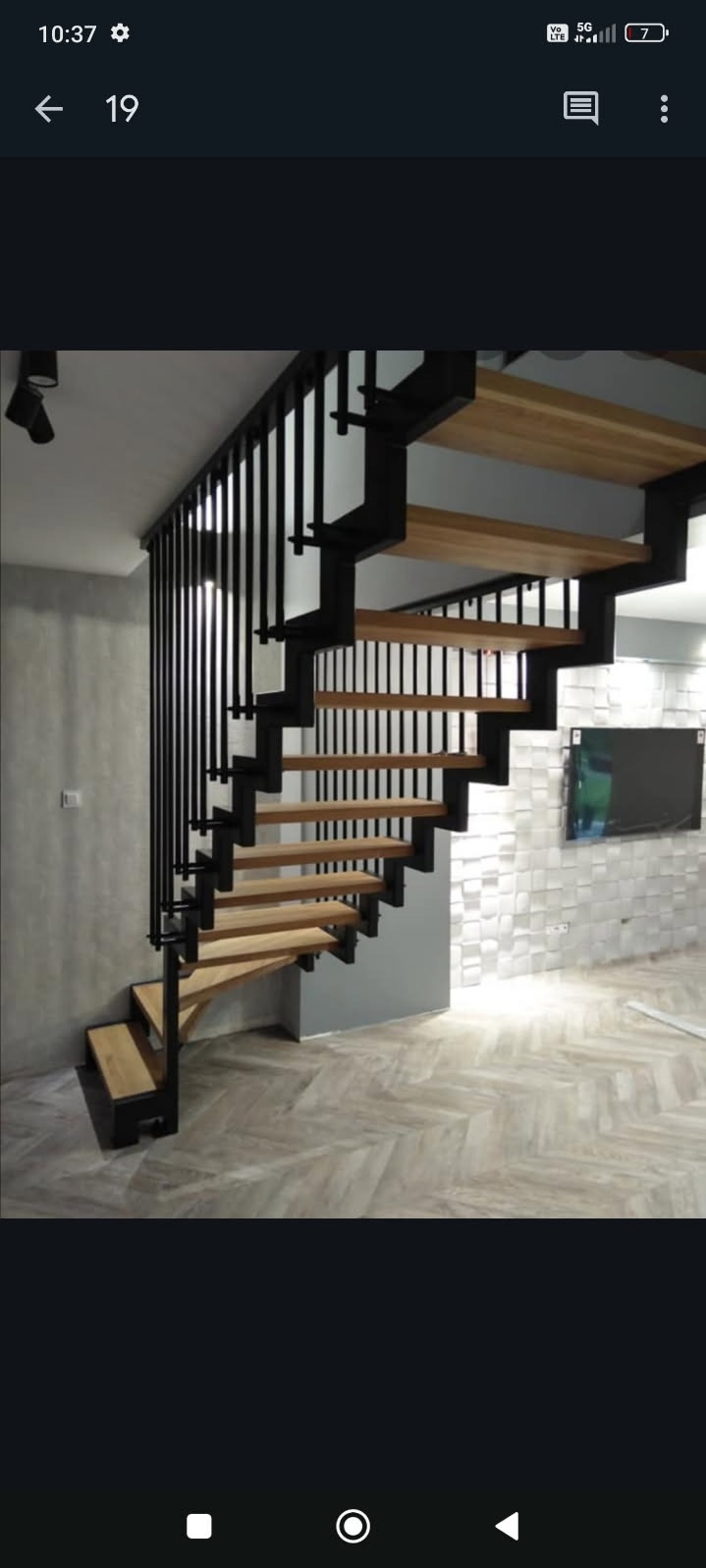 Nowoczesne schody z drewnianymi stopniami i czarną metalową balustradą. Schody spiralne, z widocznym oświetleniem i teksturą ściany w tle.