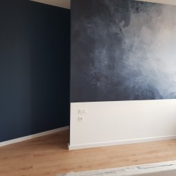 Alek Pisarczyk - Pokój po odświeżeniu: ściana w kolorze głębokiego granatu sąsiaduje z białą ścianą, nad którą znajduje się dekoracyjna malatura w odcieniach szarości i błękitu, przypominająca morski pejzaż. Jasne...