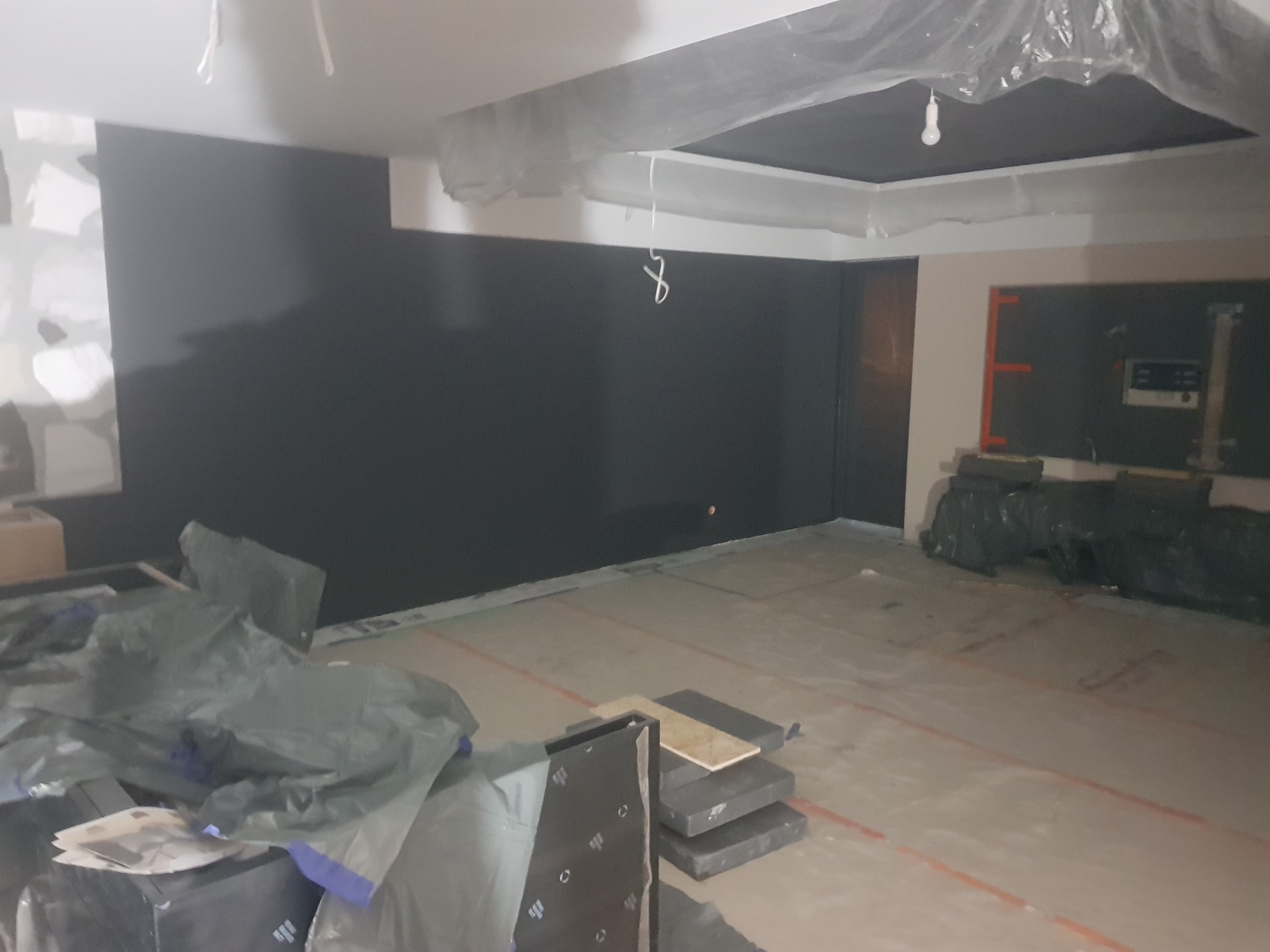 Wnętrze w trakcie prac: ściana pomalowana na ciemny grafit, folia ochronna na suficie, materiały budowlane na podłodze z widocznymi liniami poziomowania.