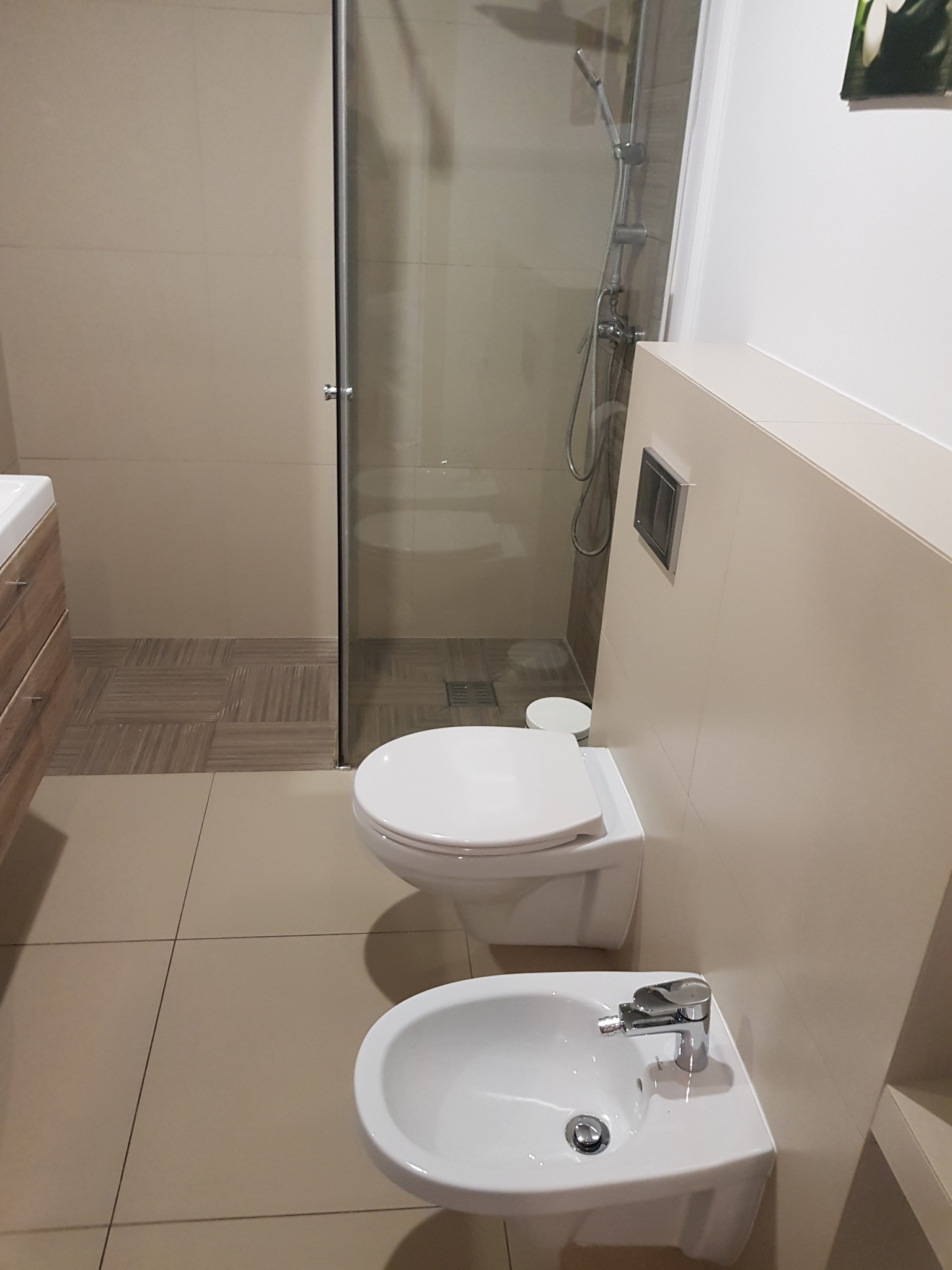 Wykończona łazienka w Krakowie z beżowymi płytkami, widoczna toaleta podwieszana, bidet i kabina prysznicowa z deszczownicą.