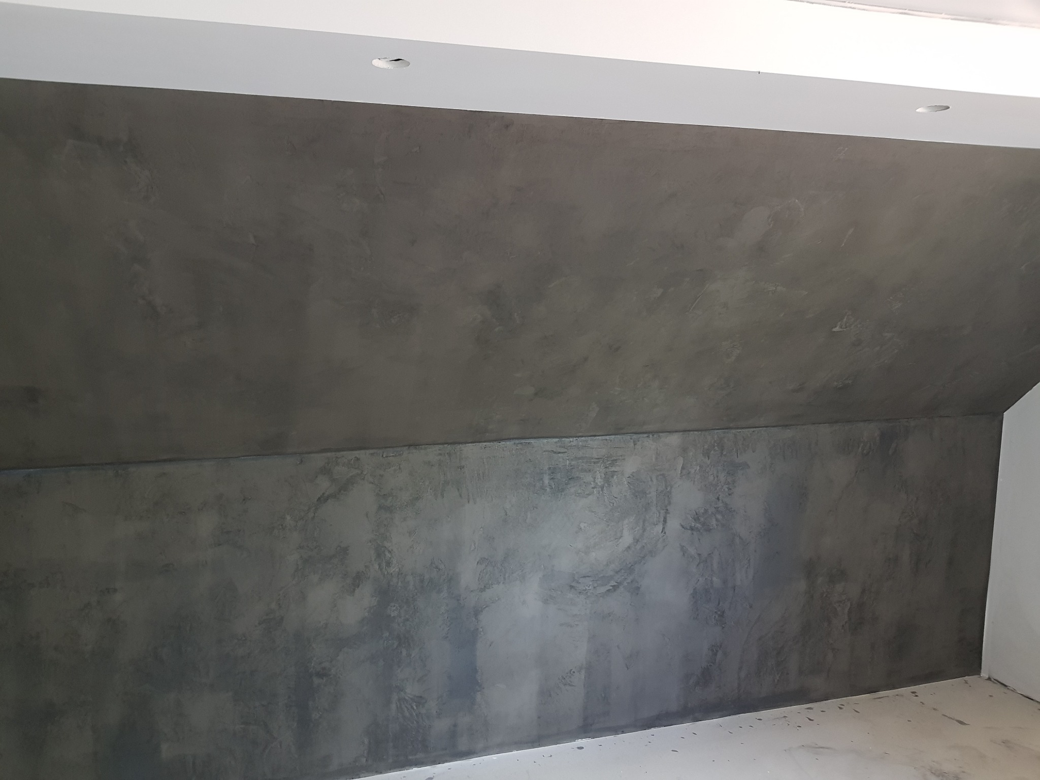 Ściana poddasza wykończona dekoracyjną szpachlą w odcieniach szarości, imitująca efekt betonu architektonicznego, widoczne nierównomierne wzory i faktura na powierzchni.