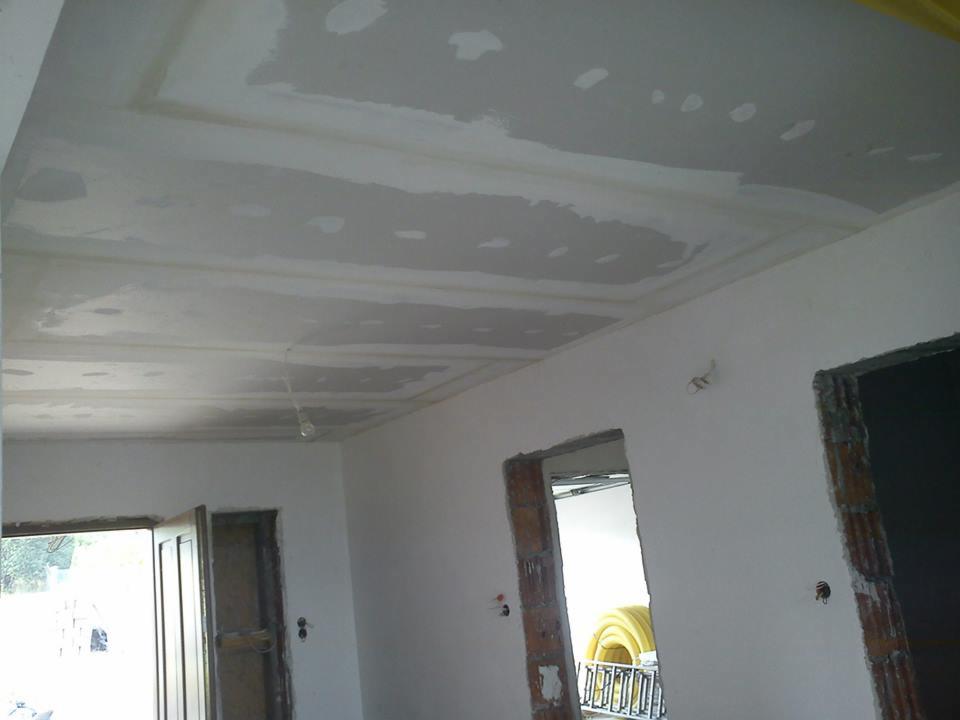 Wykończenie sufitu z płyty gipsowo-kartonowej w trakcie szpachlowania. Widoczne łączenia płyt i fragmenty ścian z otworami drzwiowymi w surowym stanie.