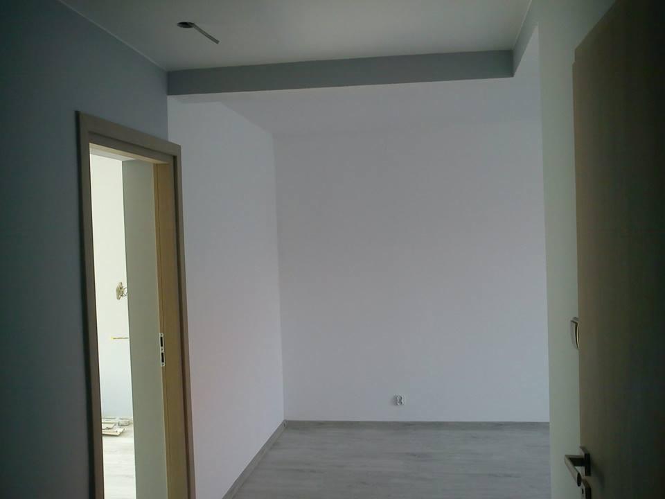 Wnętrze pokoju po malowaniu ścian na biało i szaro, z widocznymi drzwiami i fragmentem podłogi. Na suficie widoczny otwór po instalacji oświetleniowej.