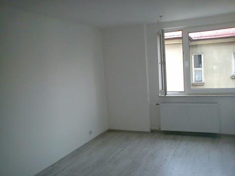 Pusty pokój po malowaniu na biało z oknem, grzejnikiem i panelami podłogowymi. Widok z perspektywy narożnika. Świeżo odnowione wnętrze mieszkania.