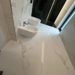 Nowoczesna łazienka wykończona białymi płytkami imitującymi marmur z widocznym bidetem i toaletą w minimalistycznym stylu, czarna ściana z oświetleniem LED, okno w górnym rogu.