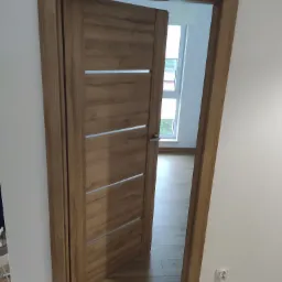 Otwarta dębowa konstrukcja z czterema poziomymi, jasnymi wstawkami, widok na jasne wnętrze z oknem i podłogą imitującą drewno.