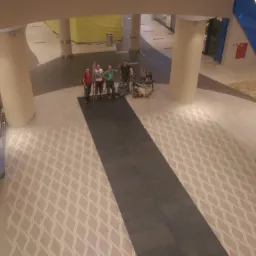 Ekipa remontowa pozuje na tle nowej podłogi w centrum handlowym, widoczny fragment posadzki z wzorem romboidalnym i eskalator.