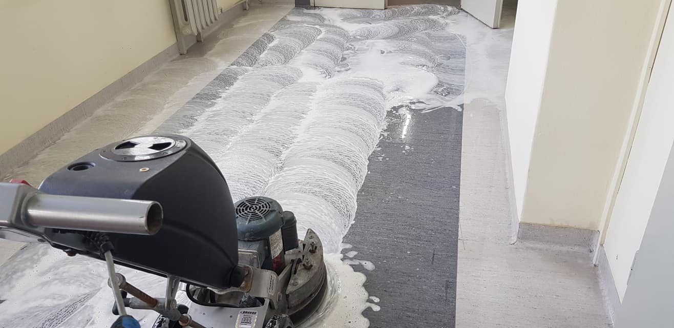 Szorowarka jednotarczowa w trakcie czyszczenia podłogi w korytarzu, widoczna piana i ślady po czyszczeniu.