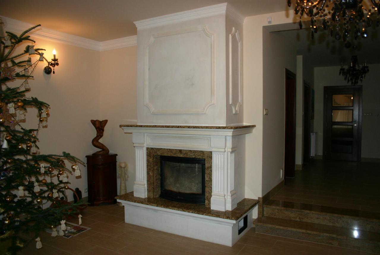 Elegancki kominek z marmurowym wykończeniem, ozdobiony kolumnami i obudową w stylu klasycznym, z elementami świątecznymi w tle.