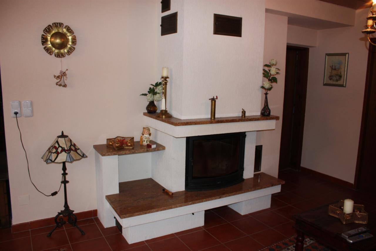 Rustykalny kominek narożny z marmurowym blatem, zdobiony figurkami i świecznikami, w ciepłym wnętrzu z lampą Tiffany i dekoracją ścienną w kształcie słońca.