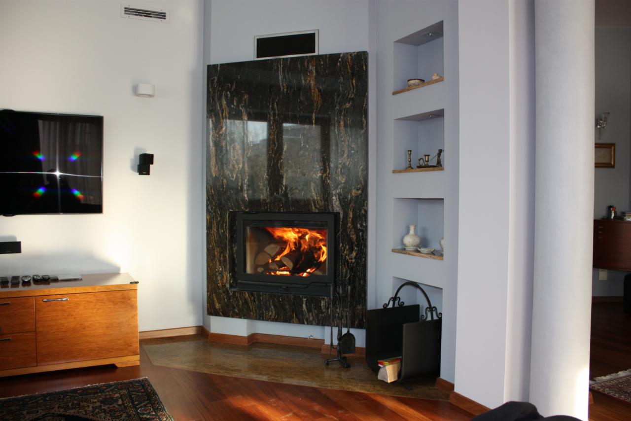 Nowoczesny kominek z czarnego marmuru z wyraźnym rysunkiem żył, płomień w palenisku, obok wnęki w ścianie z dekoracjami i metalowy stojak na drewno.