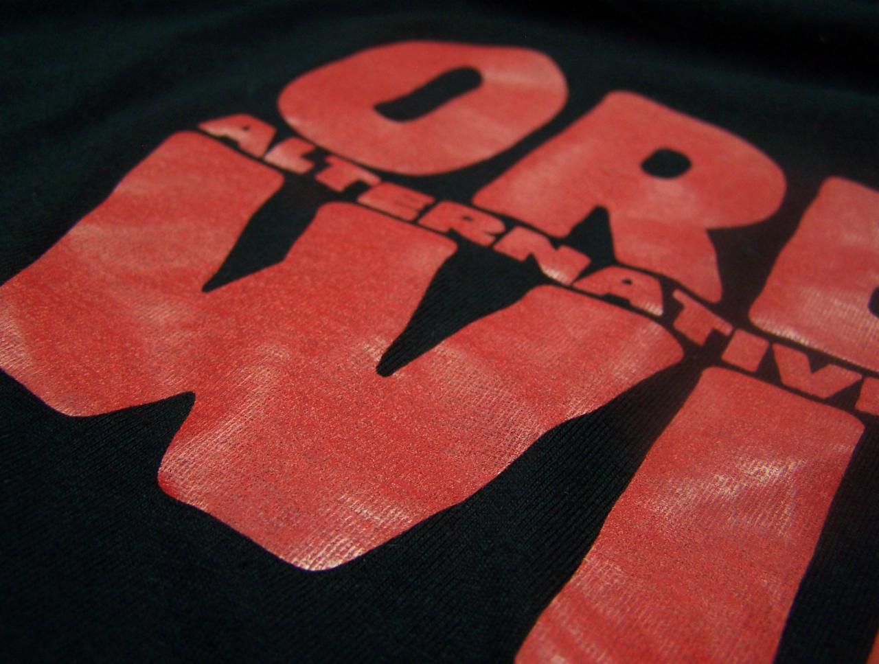 Czerwony nadruk 'WORLD ALTERNATIVE' wykonany sitodrukiem na czarnej koszulce, widoczna faktura materiału i farby.