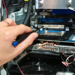 Serwisant z pierścionkiem naprawia komputer, używając wkrętaka do płyty głównej. Widoczne elementy komputera i dłoń w trakcie pracy.