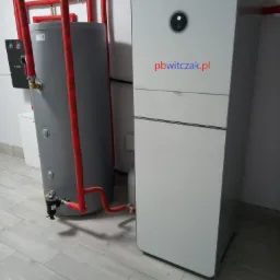 Nowoczesna instalacja grzewcza marki Bosch z zasobnikiem ciepłej wody, rurami w czerwonej izolacji i filtrem, zamontowana w pomieszczeniu z jasnymi płytkami podłogowymi.