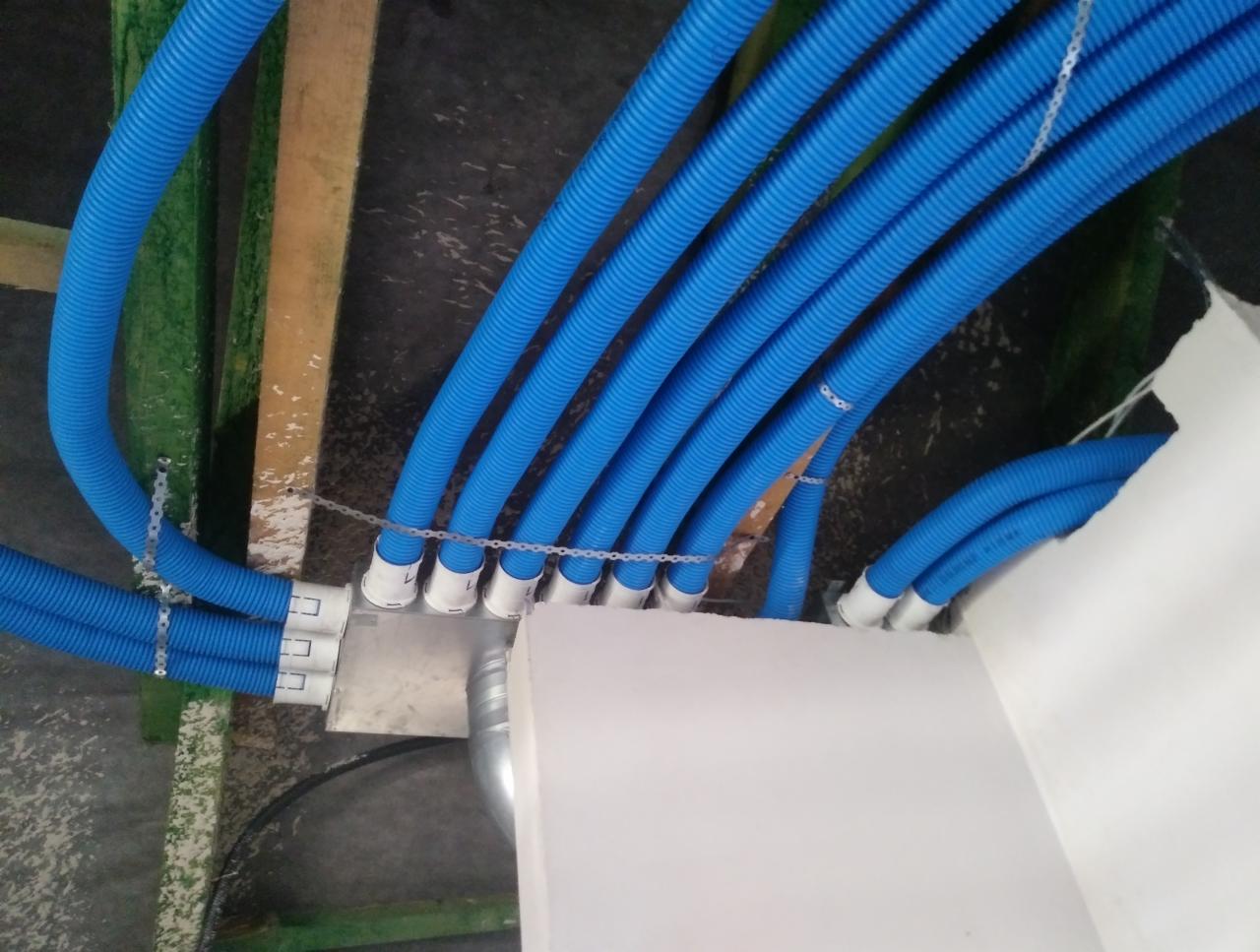 Niebieskie, karbowane rury wentylacyjne podwieszone do sufitu, połączone metalową skrzynką rozdzielczą i przymocowane perforowaną taśmą montażową.