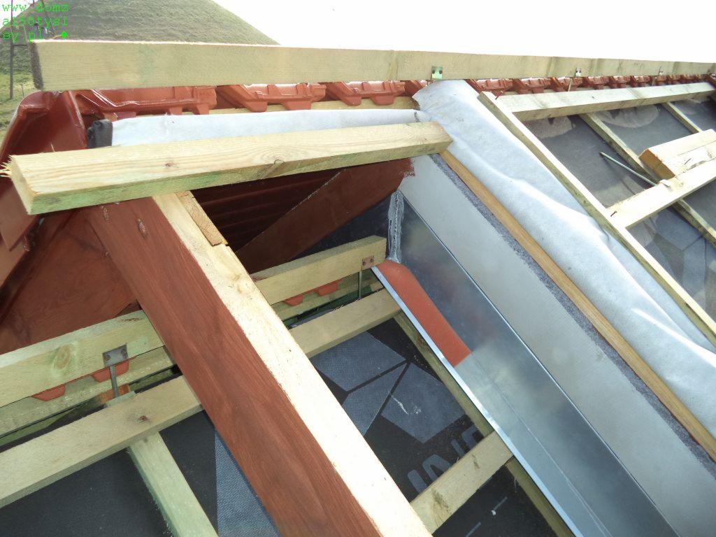 Konstrukcja dachu w trakcie krycia: drewniane krokwie, membrana dachowa, metalowe elementy, widoczne dachówki. Ujęcie z bliska na detale konstrukcyjne.