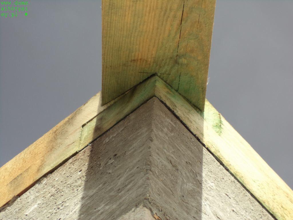 Detal konstrukcji dachu z drewnianymi elementami i szorstką, betonową powierzchnią w tle, uchwycony pod kątem z bliska.