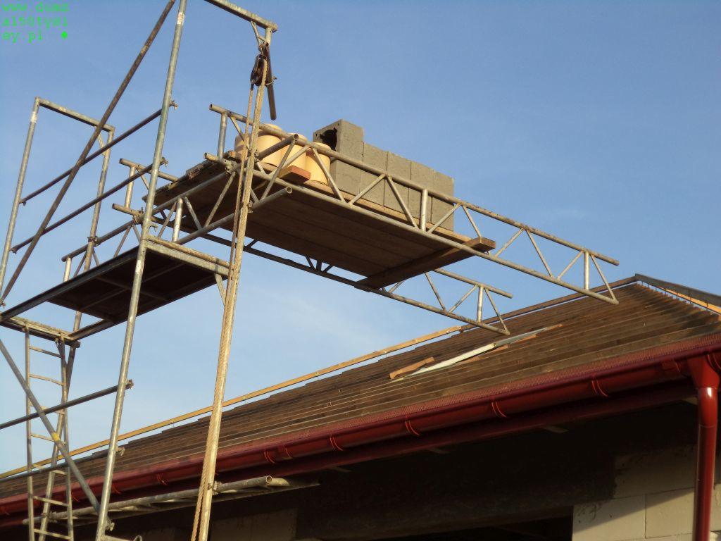 Montaż komina na dachu budynku z wykorzystaniem rusztowania w Myśliborzu. Widoczne bloczki kominowe i częściowo pokrycie dachowe z orynnowaniem.