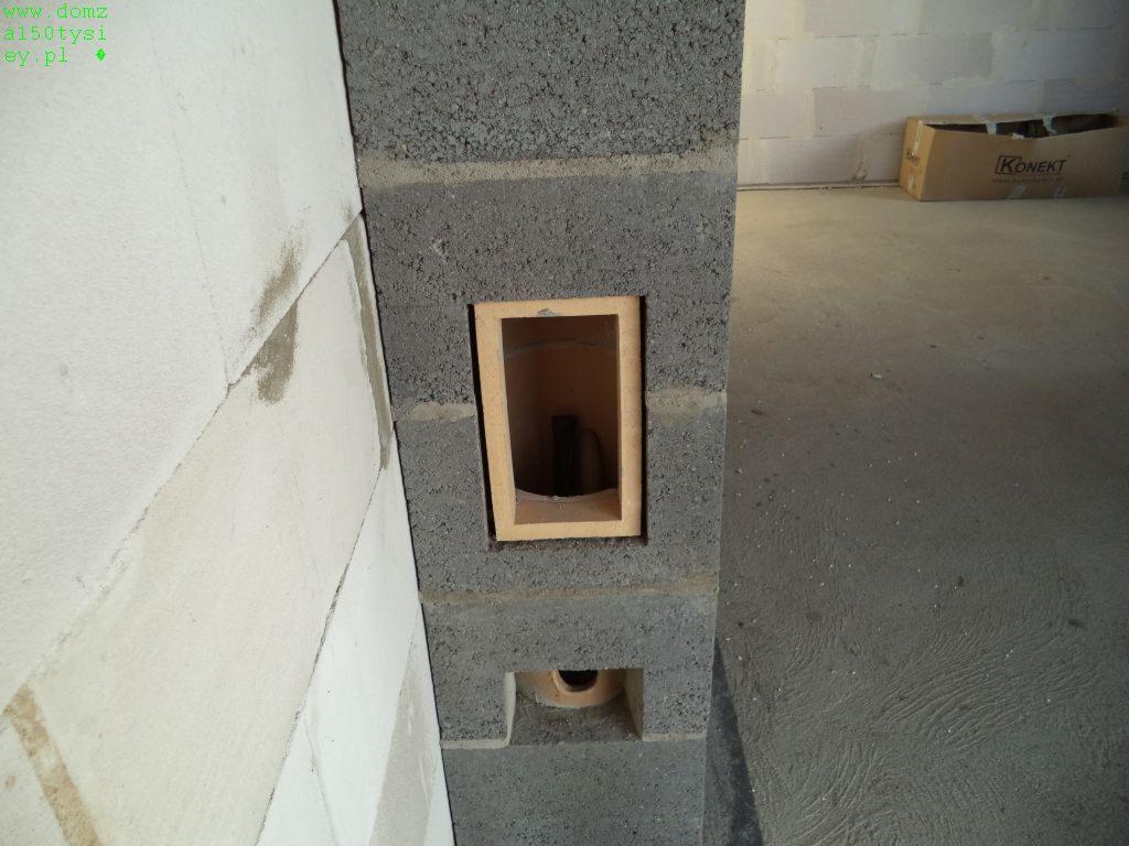 Ściana z betonu komórkowego z otworem wentylacyjnym i peszlem, surowy stan, widoczne bloczki i fuga. W tle karton. Budowa domu w trakcie realizacji.