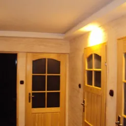 Wykończone wnętrze: drewniane drzwi z szybami, ściany z dekoracyjną fakturą i listwa sufitowa. Ciepłe oświetlenie podkreśla detale wykończenia.