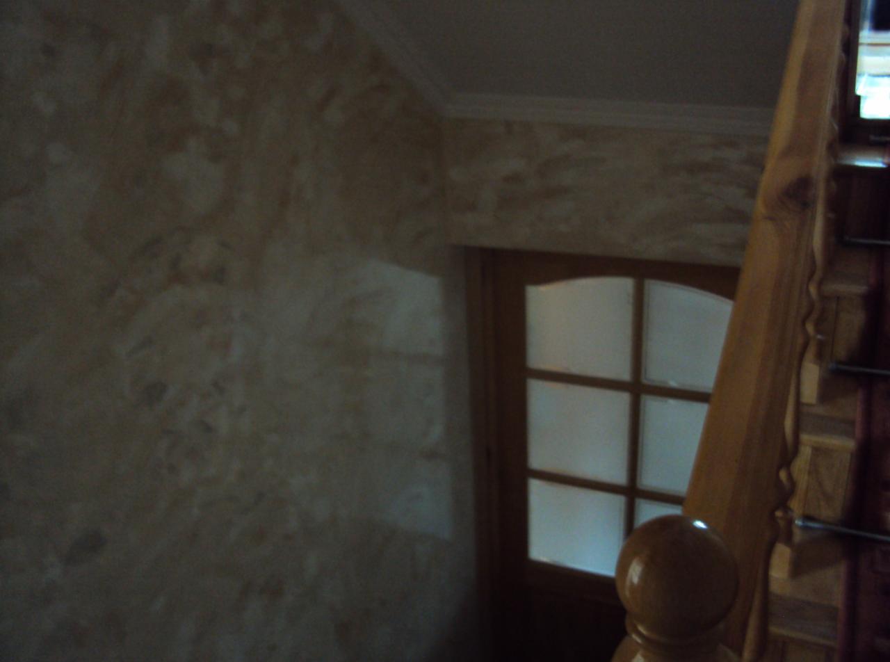 Ściana z efektem dekoracyjnym w odcieniach beżu, drewniane schody i okno z szybami mlecznymi w tle. Widok z góry, wnętrze domu.