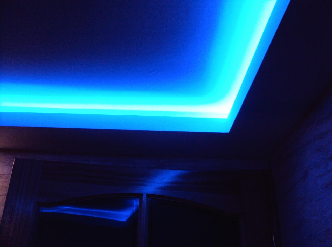 Nowoczesny sufit podwieszany z oświetleniem LED w odcieniach niebieskiego, widoczny fragment ściany i drzwi. Efektowne doświetlenie pomieszczenia.