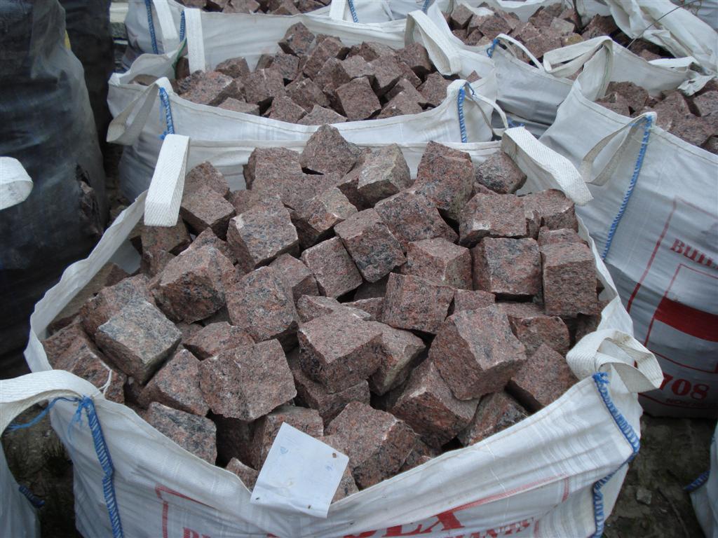 Worek typu Big Bag wypełniony kostką z czerwonego granitu o nieregularnych kształtach, widoczne inne worki w tle.
