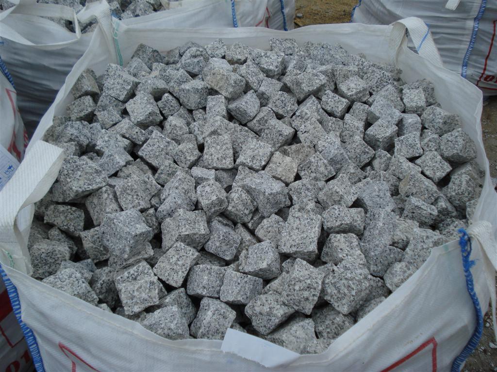 Worek typu Big Bag wypełniony szarą kostką brukową o porowatej strukturze, widoczne fragmenty innych worków w tle.
