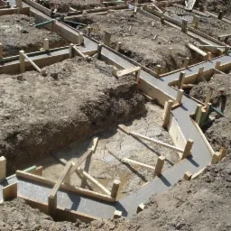 Zalane betonem, drewniane szalunki fundamentów w wykopie. Widoczne zbrojenia. Ujęcie z góry, jasne oświetlenie.