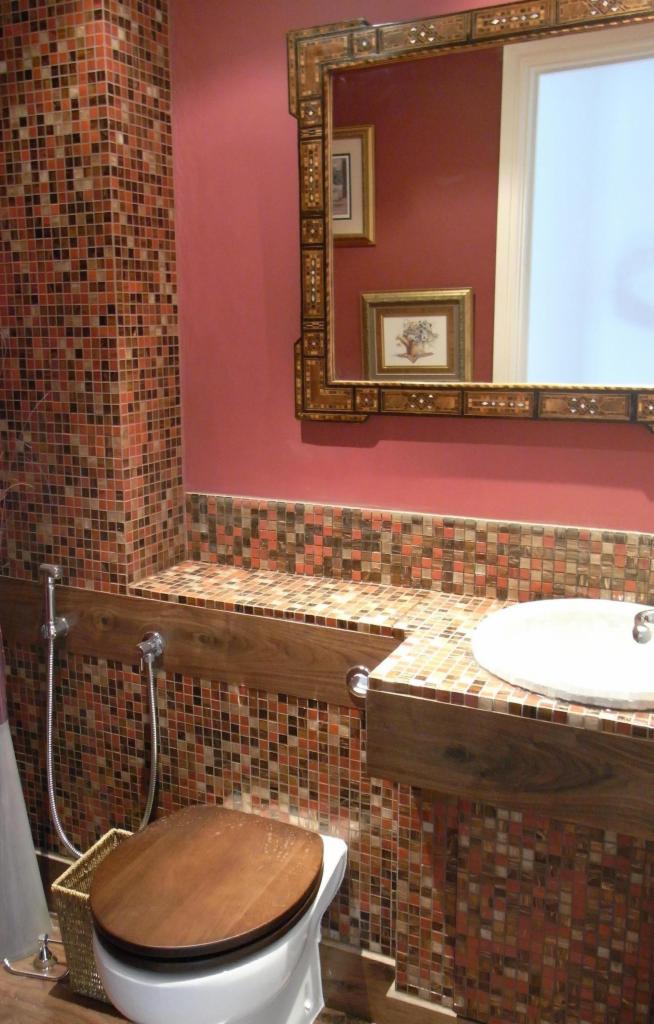 Mozaika w łazience w odcieniach brązu i pomarańczy, drewniana deska sedesowa i rama lustra. Umywalka z baterią. Detal wykończenia wnętrza.
