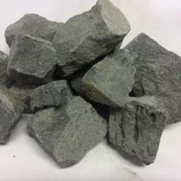 Gromadą ułożone bryły szarego, porowatego materiału na jasnym tle. Widoczne nieregularne kształty i tekstura.