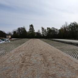 Przedsiębiorstwo Budowlano Transportowe Stefan Zakrzewski - Widok z perspektywy ziemi na plac z ułożoną ażurową kostką brukową, częściowo zasypaną piaskiem, w tle drzewa i błękitne niebo.