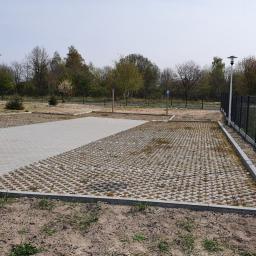 Przedsiębiorstwo Budowlano Transportowe Stefan Zakrzewski - Nowo wybudowany parking z kostki brukowej ażurowej i pełnej, z widocznymi obrzeżami, słupami oświetleniowymi i ogrodzeniem panelowym, na tle budynku mieszkalnego i drzew.