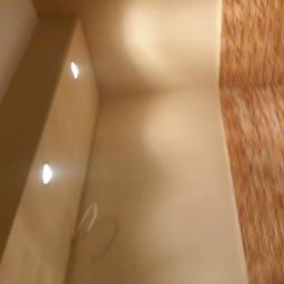 Usługi Ogólnobudowlane Adam Bednarski - Ściana z gładzią w odcieniach beżu, oświetlona dwoma punktowymi lampami LED, sąsiadująca z fragmentem ściany wykończonej okładziną imitującą drewno.