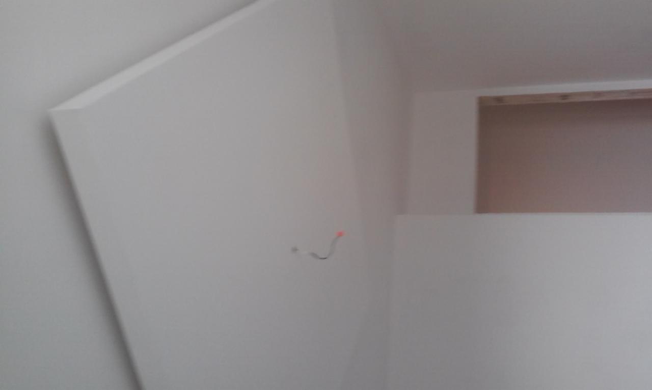 Ściana z zamontowaną płytą karton gips, widoczny przewód elektryczny wystający ze ściany i fragment drewnianej konstrukcji w tle