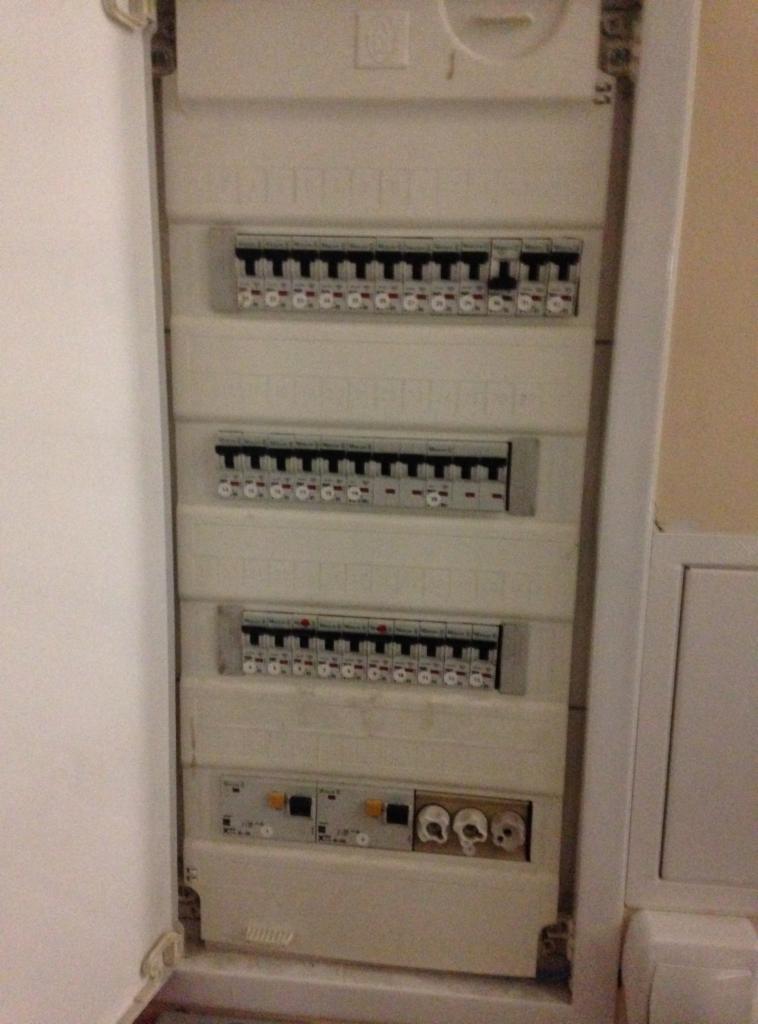 Otwarta, biała skrzynka rozdzielcza z bezpiecznikami i wyłącznikami, widoczne okablowanie. Widok z bliska, oświetlenie pomieszczenia.
