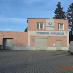 Budynek magazynowy z napisem 'CENTRUM NARZĘDZI' i logo STEM, widok z zewnątrz, zaparkowany srebrny samochód dostawczy z logo firmy.