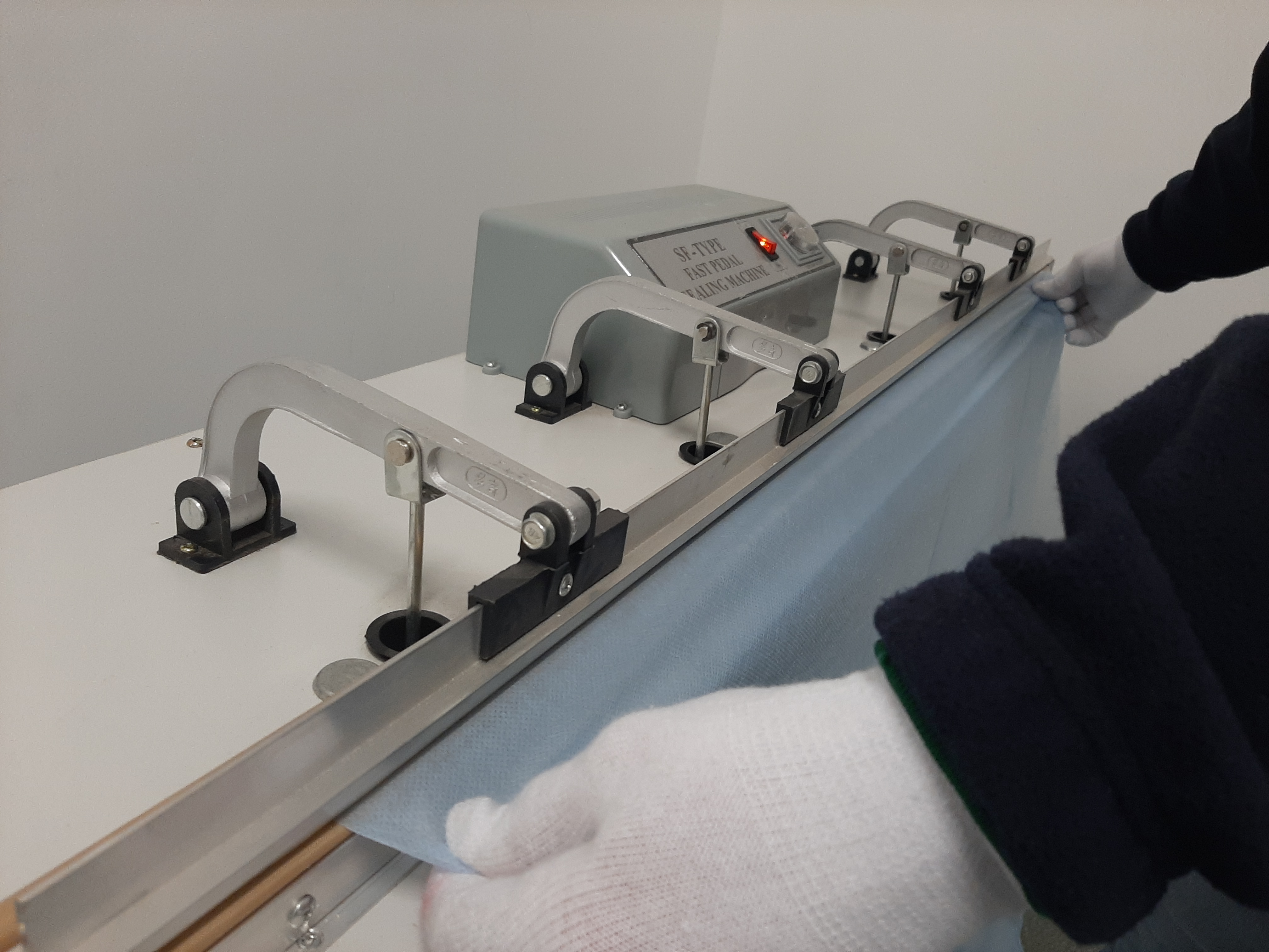 Operator w białych rękawiczkach obsługuje maszynę do zgrzewania folii z czerwoną diodą, przygotowując materiał do zgrzewu.