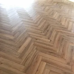 Ułożona podłoga z paneli w jodełkę francuską, widok z góry, jasne wnętrze z dużym oknem.