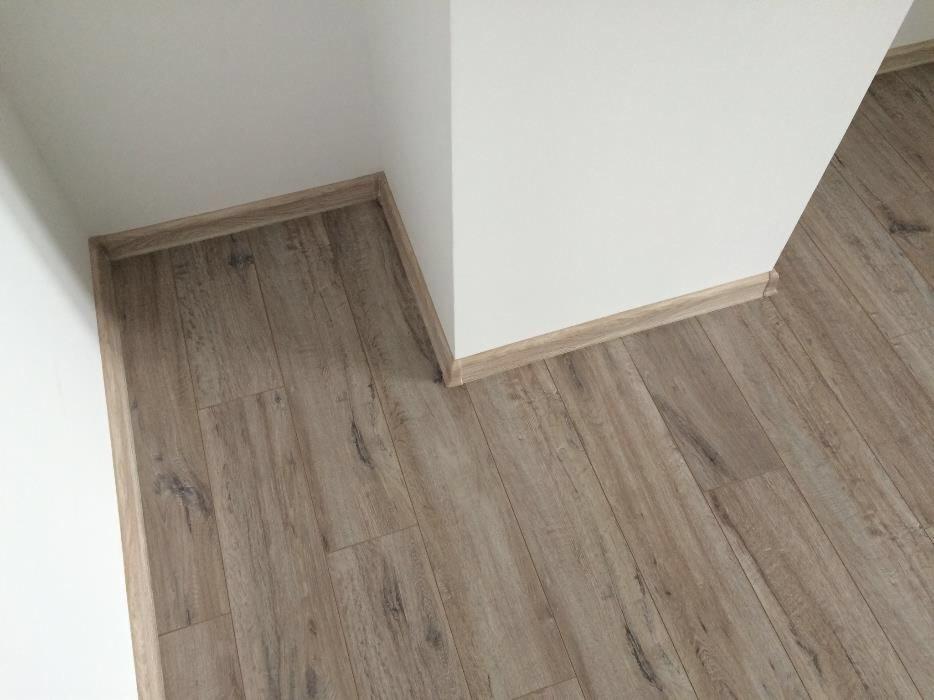 Ułożone panele podłogowe w rogu pomieszczenia, widoczne listwy przypodłogowe w kolorze paneli.