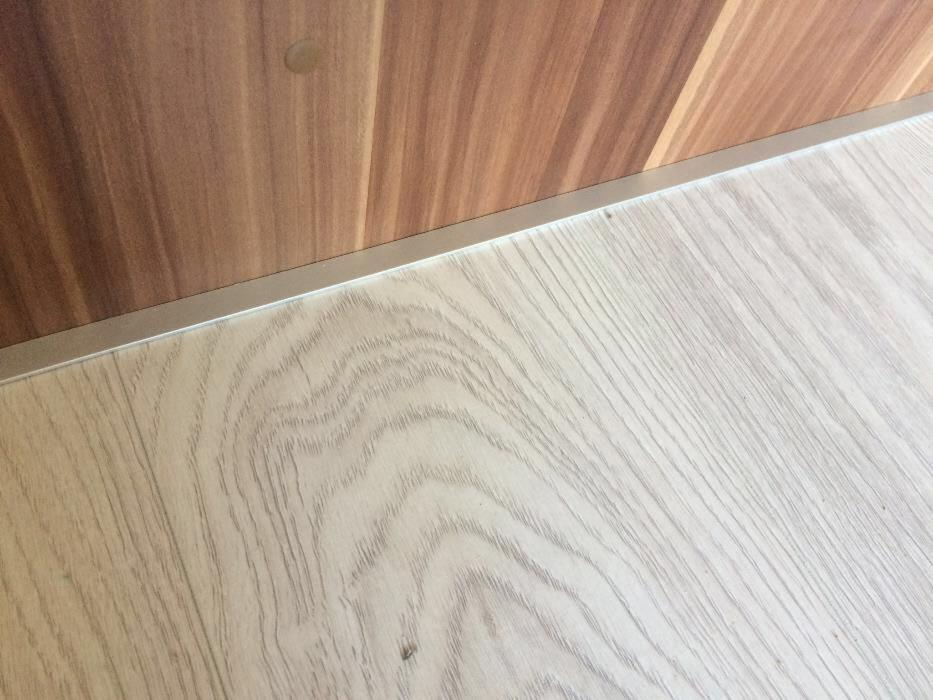 Jasna podłoga panelowa z widocznym wzorem drewna i listwą przypodłogową w kolorze orzecha.