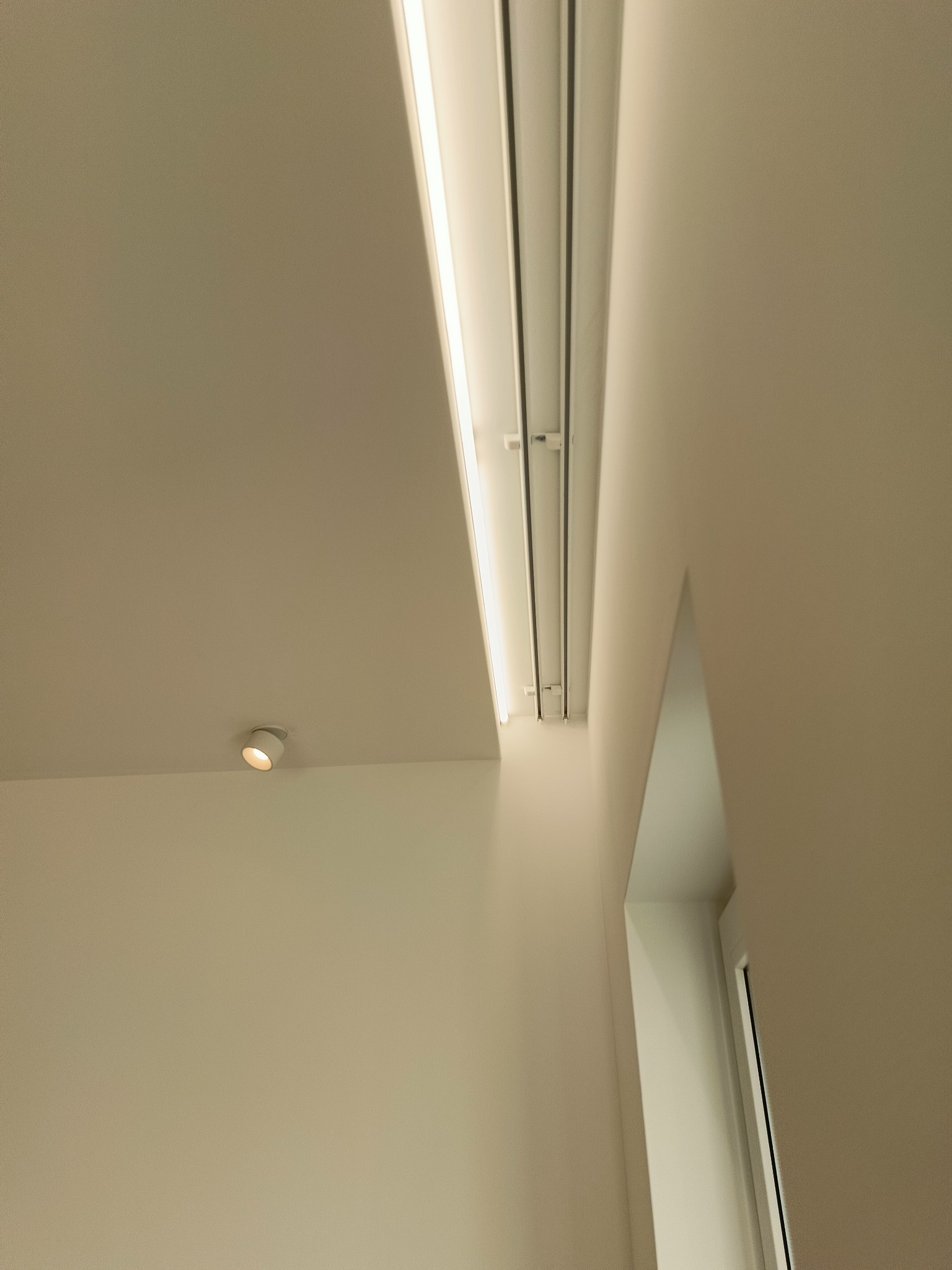 Minimalistyczne oświetlenie sufitowe z szynoprzewodem i reflektorem punktowym w nowoczesnym wnętrzu z jasnymi ścianami i drzwiami.