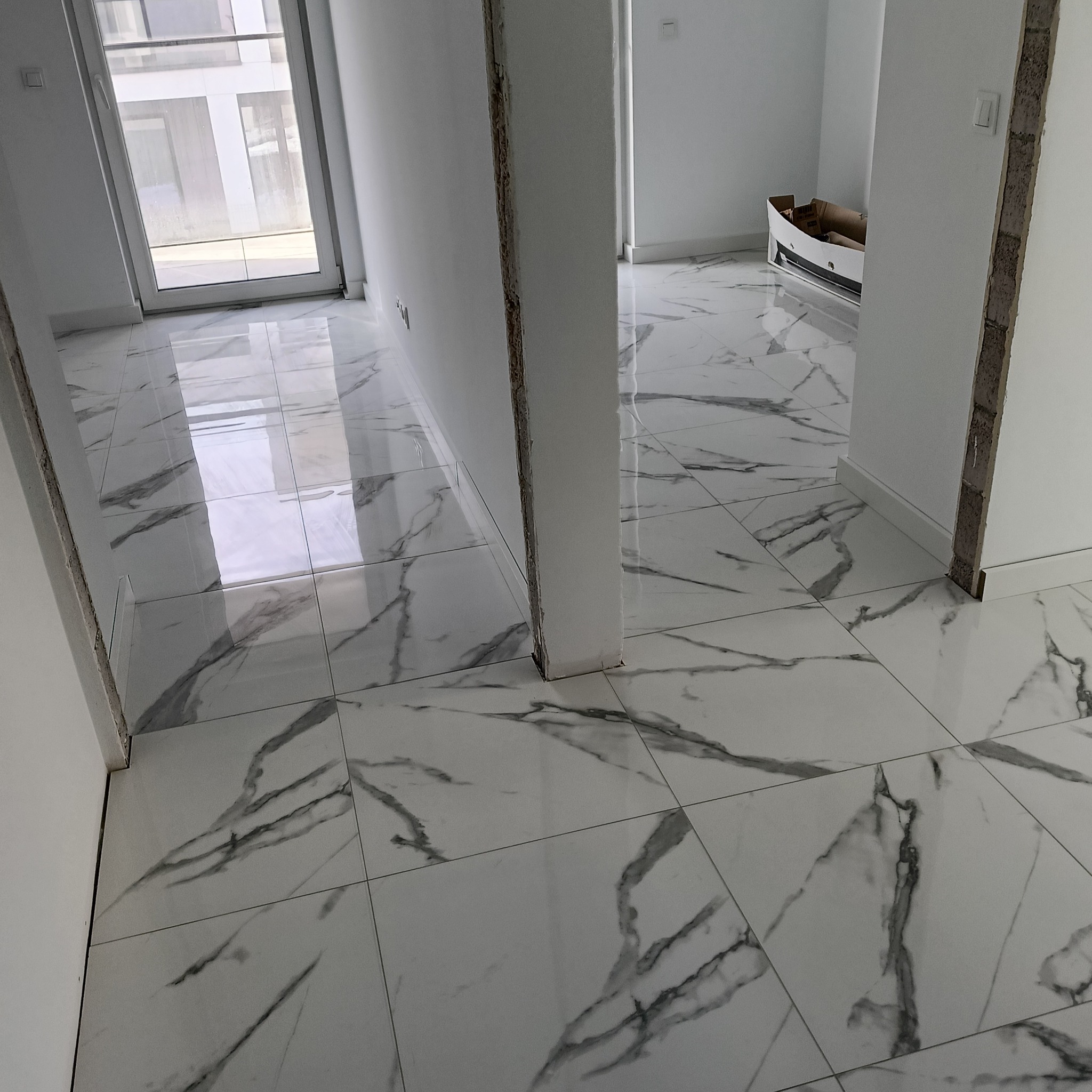 Błyszcząca, biała podłoga z marmurowym wzorem w jasnym wnętrzu. Widoczne niedokończone wykończenia ścian i podłogi. Nowoczesny design i jasne kolory.