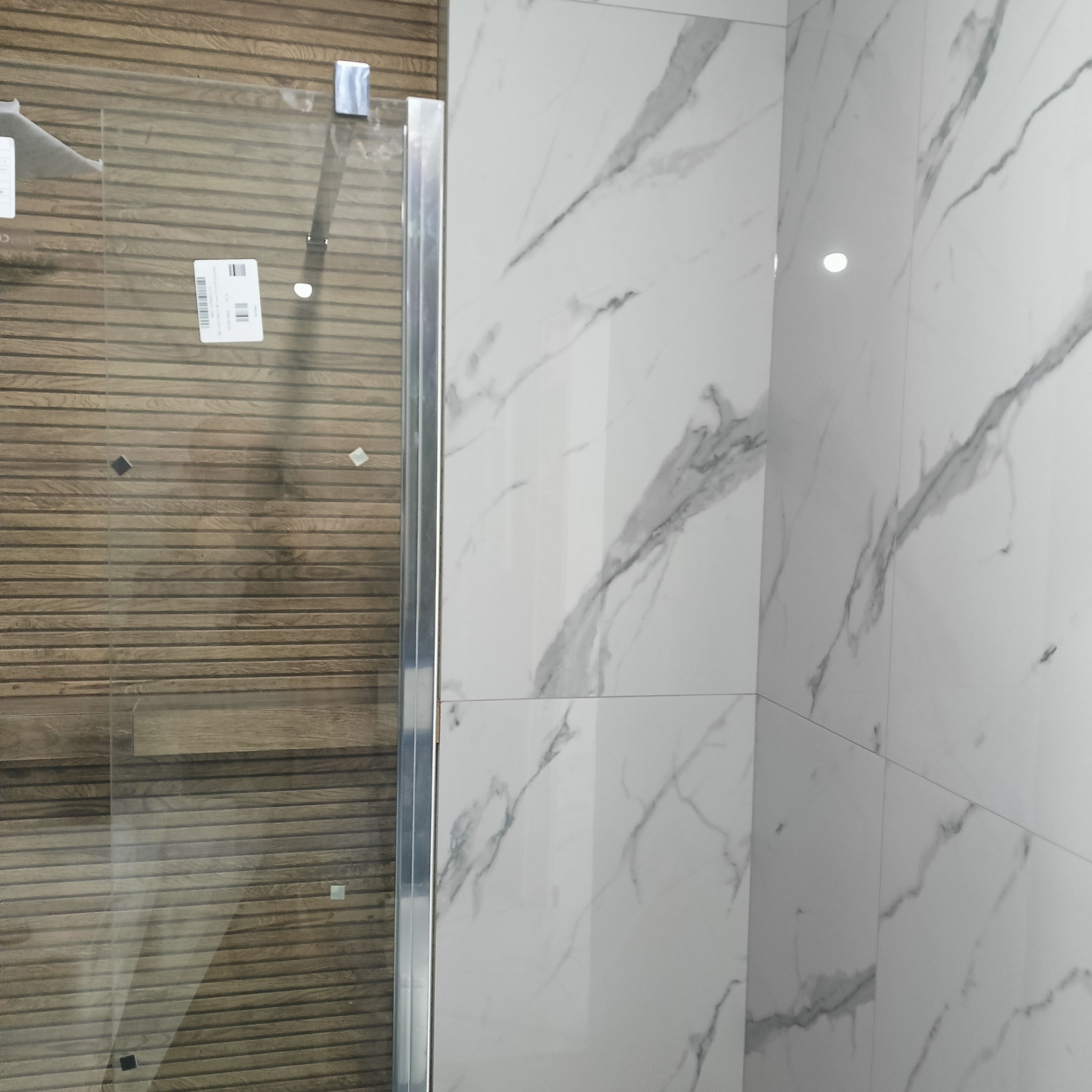 Wykończona kabina prysznicowa z marmurowymi płytkami i drewnopodobną okładziną. Nowoczesny design, minimalistyczne wykończenie.