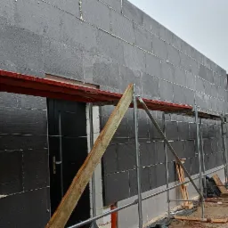 Dom w trakcie ocieplania elewacji styropianem grafitowym, widoczne rusztowania, boczny widok na budynek z zamontowanymi panelami fotowoltaicznymi w tle.