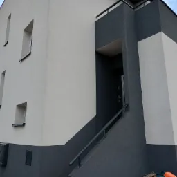 Nowoczesny dom z dwukolorową elewacją w odcieniach szarości i bieli, z widocznym wejściem i schodami z barierką.