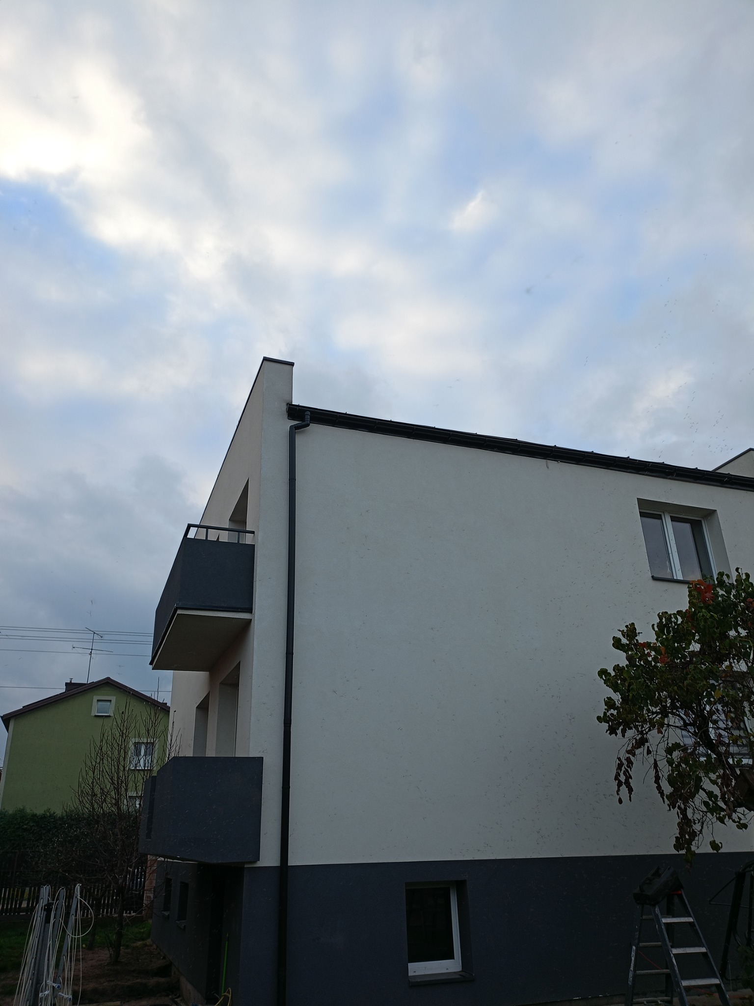 Dwukondygnacyjny dom z balkonem w Turku, po remoncie elewacji, z widoczną drabiną i fragmentem zieleni.