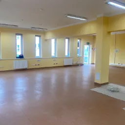 Przygotowane do malowania, puste pomieszczenie biurowe z żółtymi ścianami, brązową podłogą, grzejnikami pod oknami i puszką farby na podłodze.