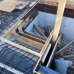 Budowa schodów żelbetowych w piwnicy domu w Gryficach. Widoczne zbrojenie, szalunki i pracownik w trakcie montażu konstrukcji.