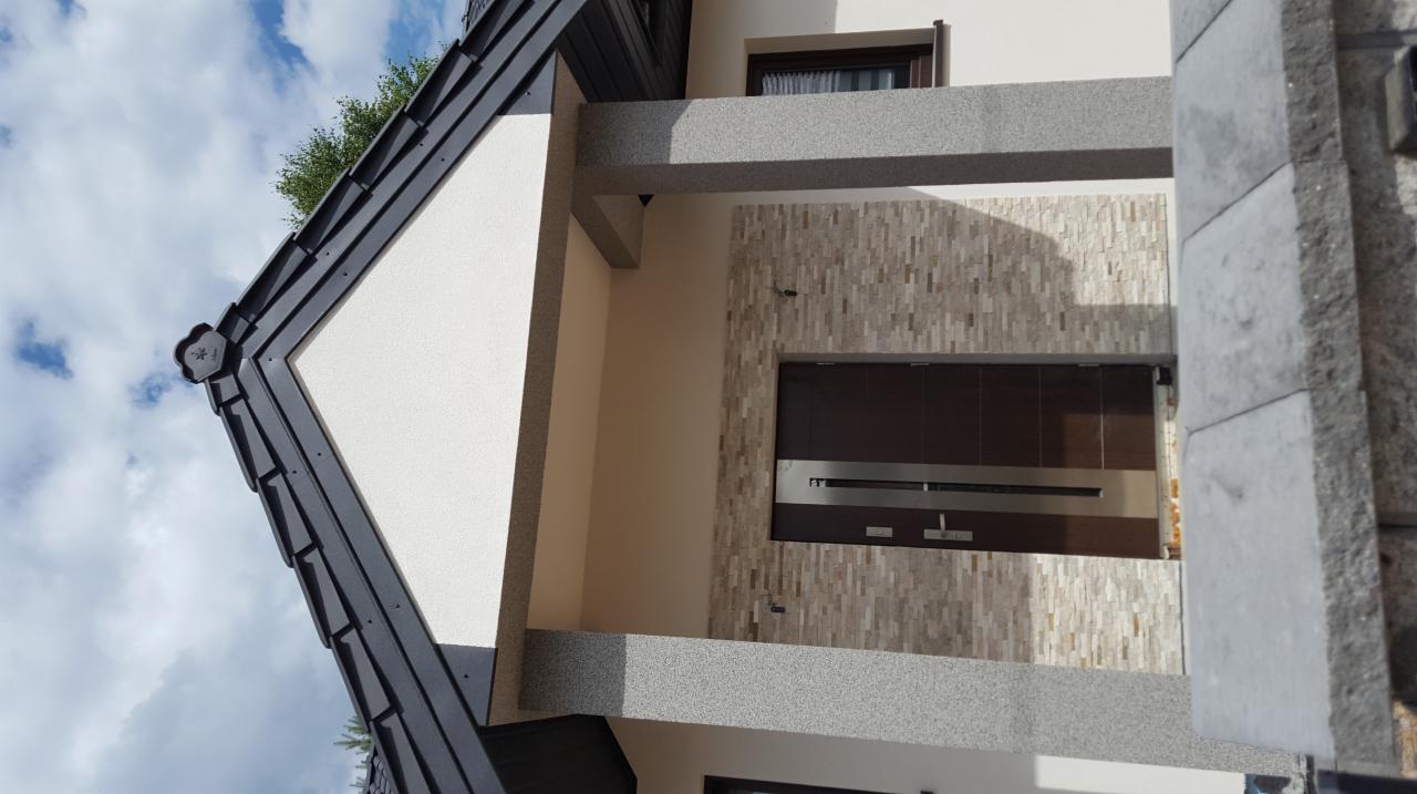 Nowoczesny dom z jasną elewacją, kamienną okładziną przy wejściu i grafitową dachówką, widok z dołu na fragment fasady i niebo.